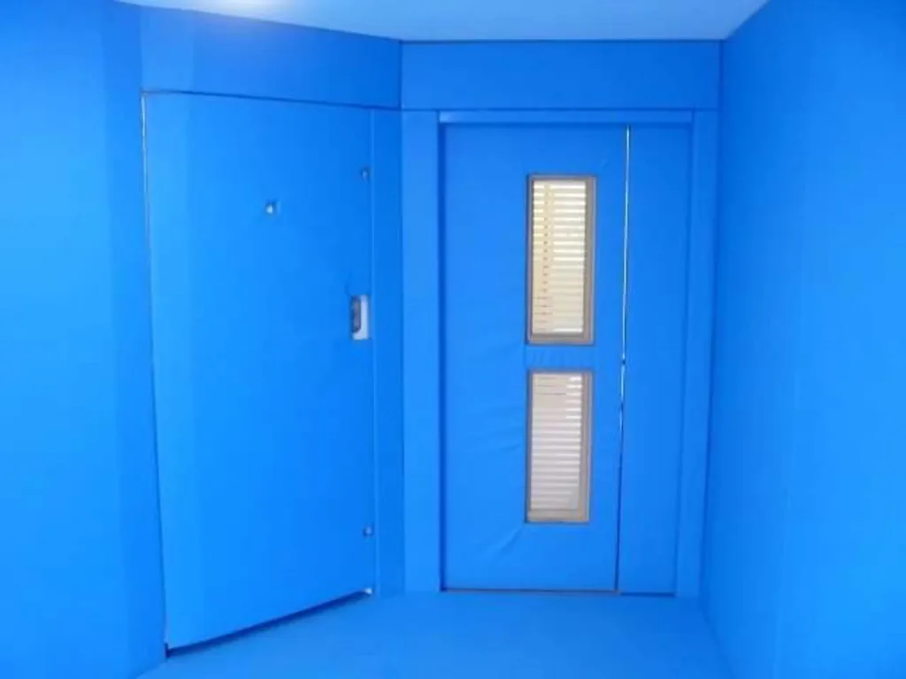 Bespoke control and restraint room interior with blue padded walls and a padded door featuring two narrow glazed panels with blinds.
