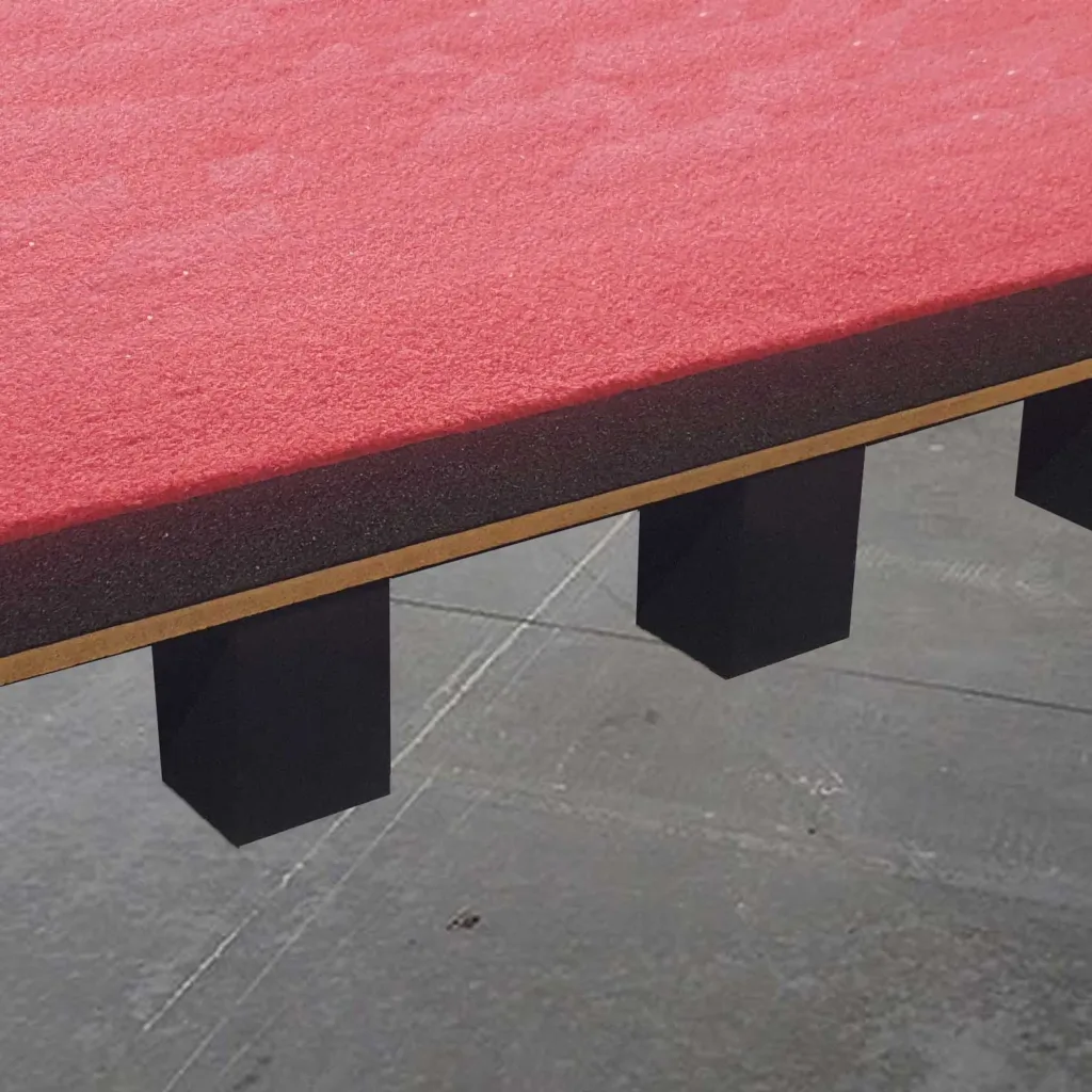 Sprung floor section with a red carpeted top, dark foam and plywood edge, and black closed-cell PE foam support blocks beneath.