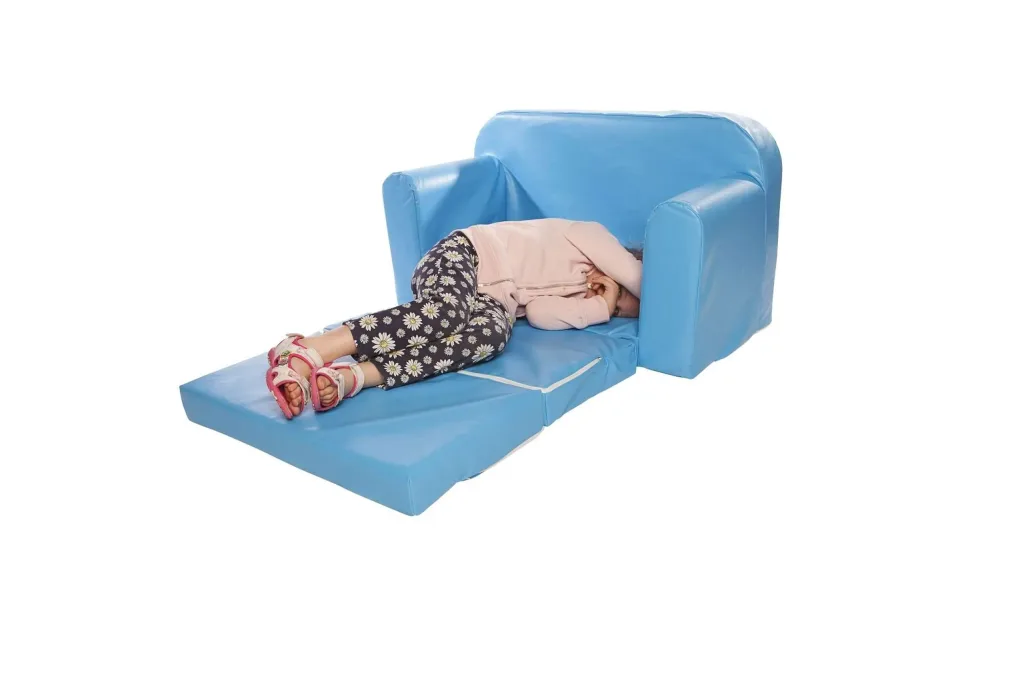 Child curled up on an unfolded light blue PVC sofa bed with armrests, wearing a pink jacket, daisy-print pants and pink sandals.
