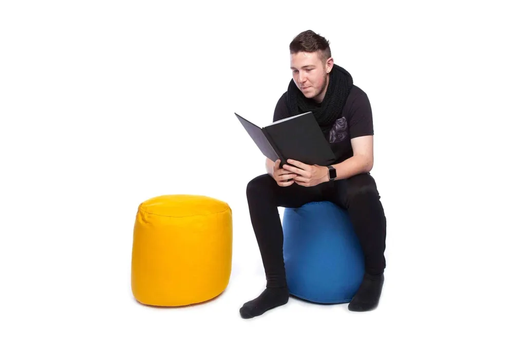 Man sitting on a sky blue cotton bean pouffe reading a book, with a yellow cotton bean pouffe beside him.