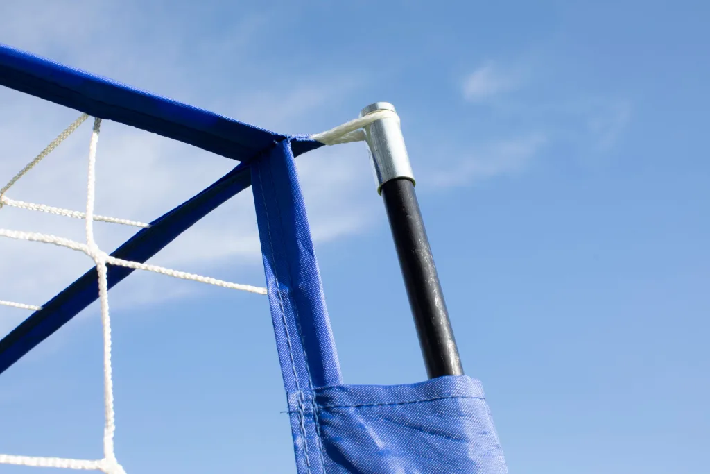Blue padded goal corner with white netting tied to a black pole against a clear blue sky.