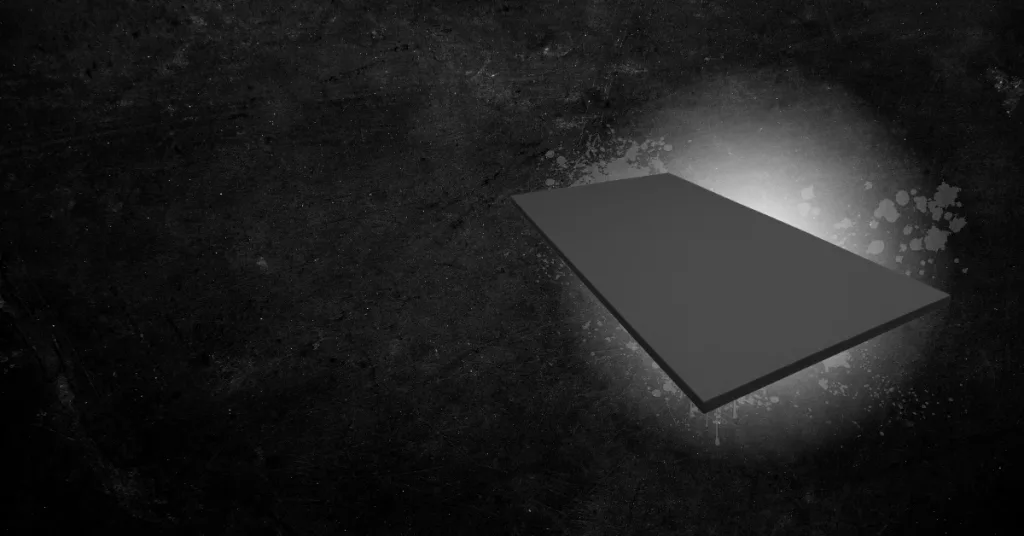 Dark gray rectangular mat tilts upward in the right foreground over a black grunge background with white splatter and halo light.