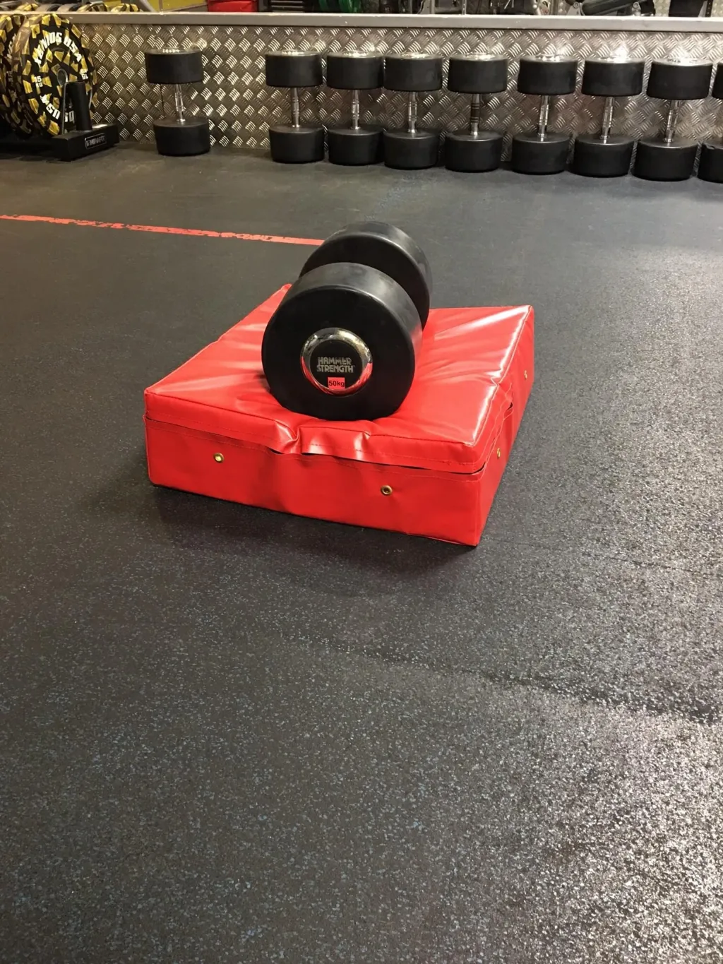Red weightlifting drop pad in fire-retardant PVC with a black dumbbell labeled HAMMER STRENGTH 50kg resting on top.