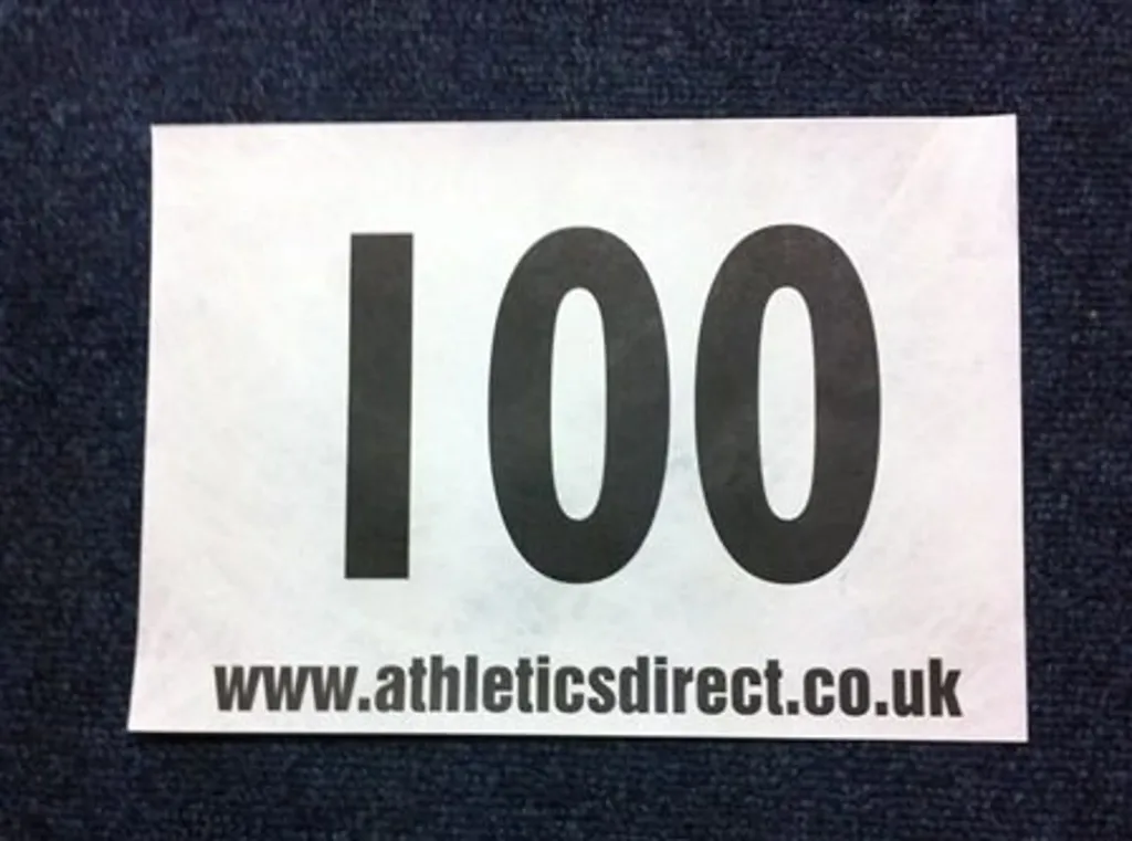 Race number showing large black 100 printed on a white rectangle against a dark fabric background.