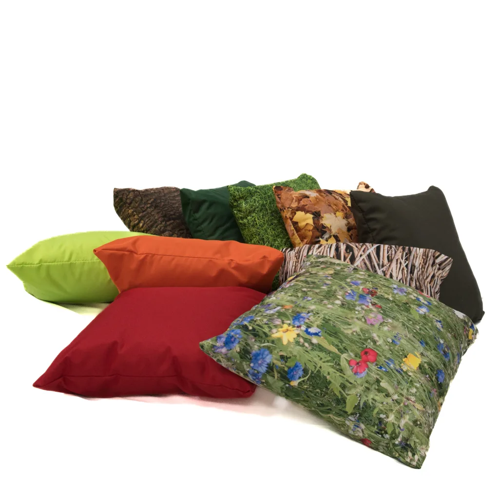 Set of ten nature-print and solid-color scatter cushions arranged in a casual pile, featuring floral, grass, autumn leaf and bark prints.