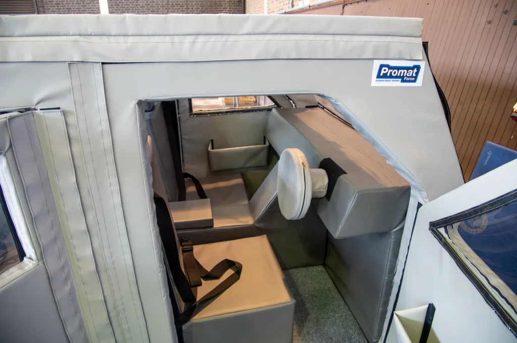 Gray PVC-covered training car interior with foam seats, seatbelt, round foam steering pad and sticker reading Promat Force.