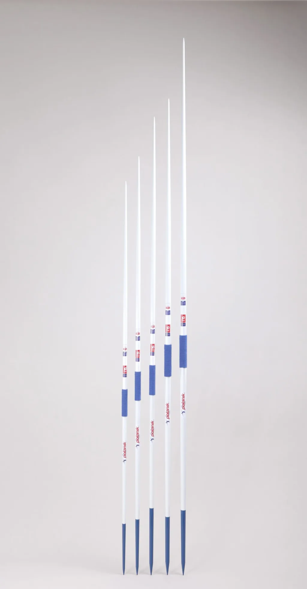 Five white training javelins with blue hand grips and blue steel heads standing upright against a light gray background.