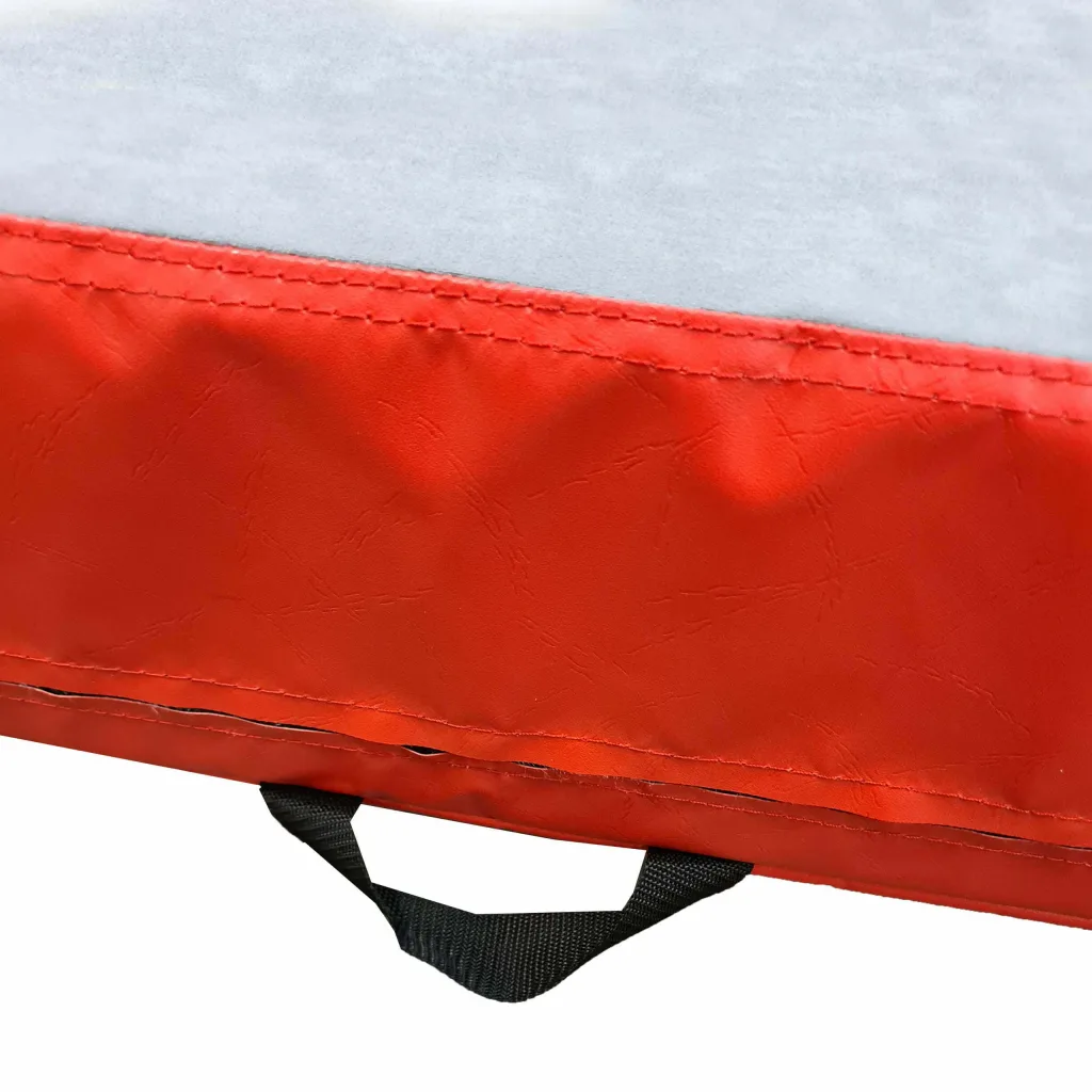 Close-up of a crash mat edge showing grey jersey fabric top, red PVC side with stitched seam and a black carry handle.