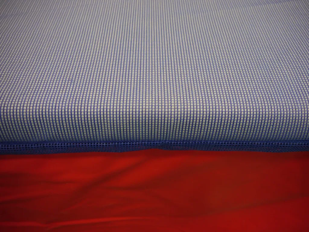 Blue woven spike proof mesh wearsheet layered over red foam landing pad with a visible edge seam.