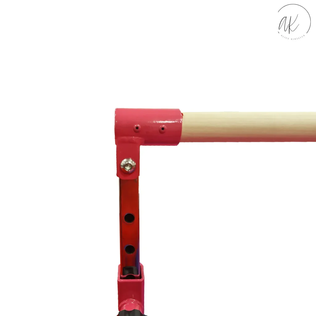 Pink adjustable high bar support with a light wood horizontal bar, height-adjustment holes, and logo text "ak" "ALICE KINSELLA".