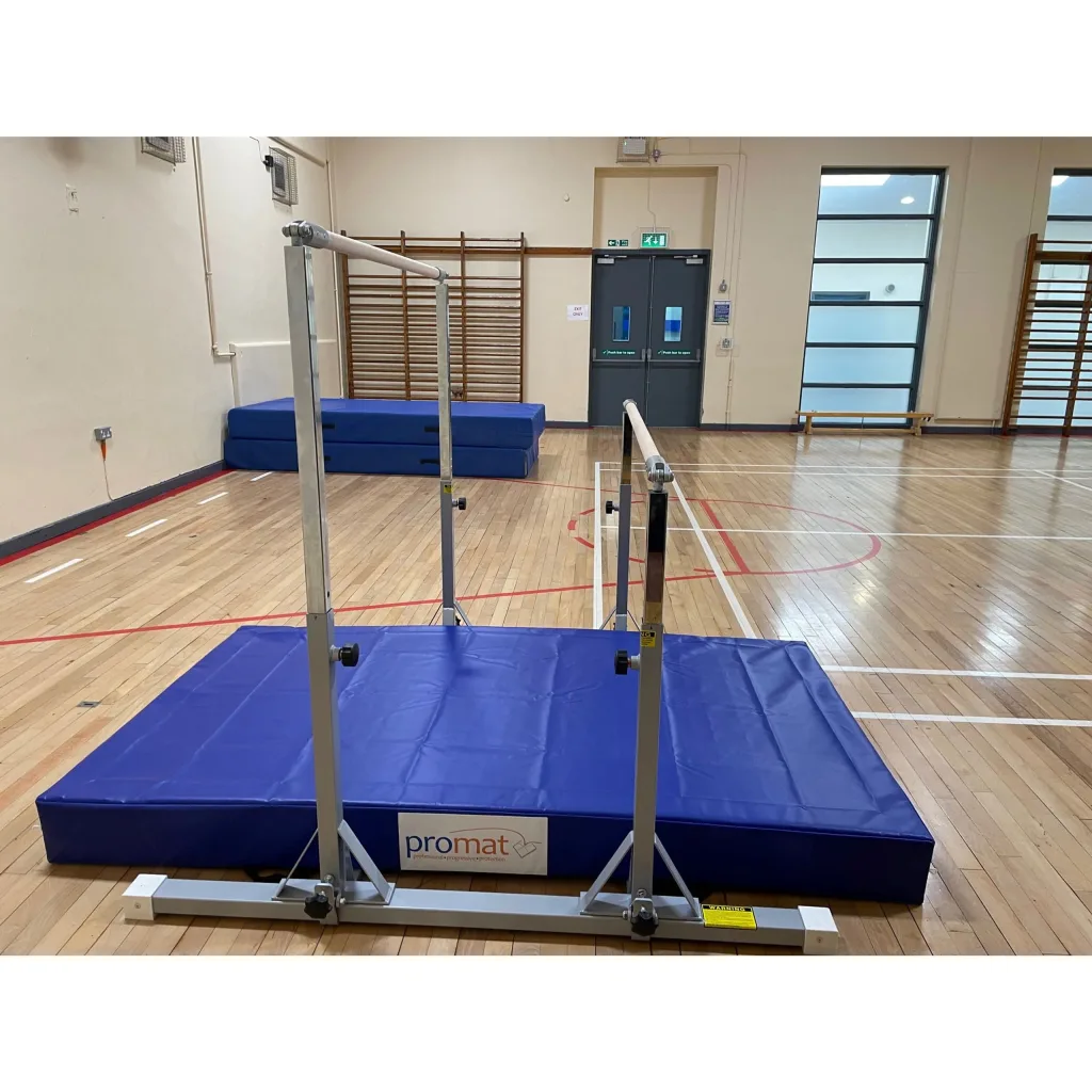 Taishan kids uneven bars with silver metal frame over a blue crash mat labeled promat, placed on a wooden gym floor.