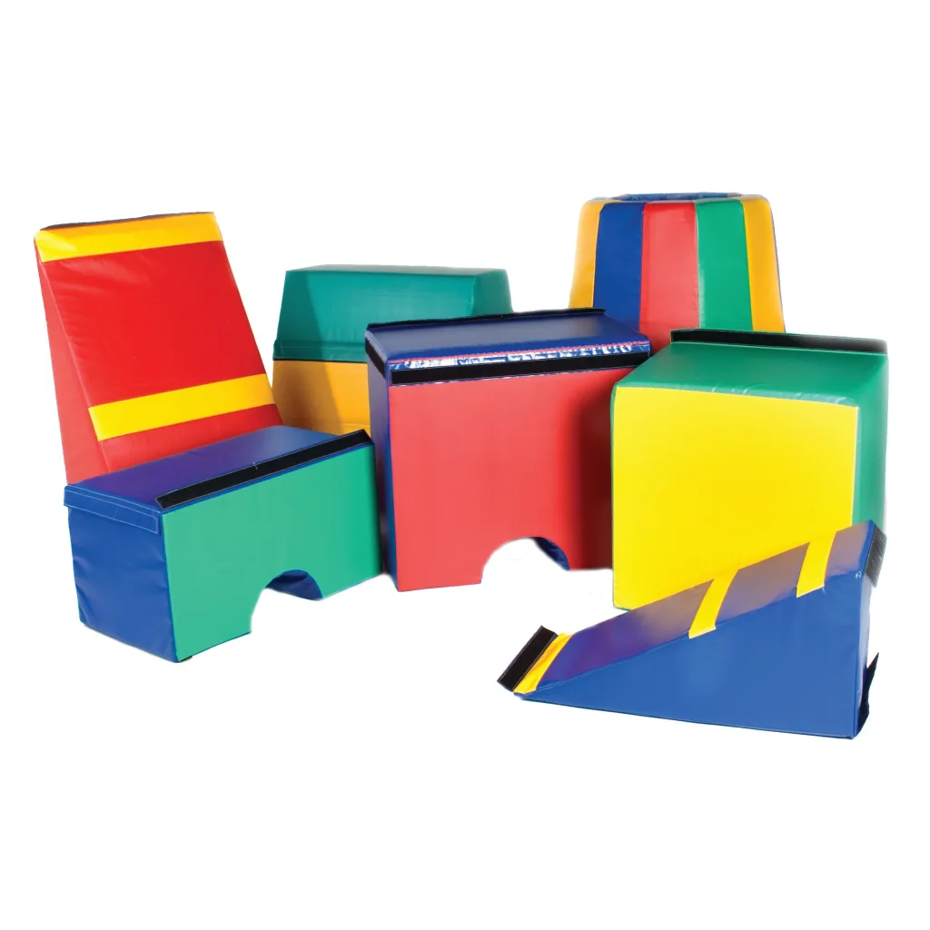 Colorful soft foam gymnastics blocks, wedges and ramps in red, yellow, green and blue arranged as a children's gym set.