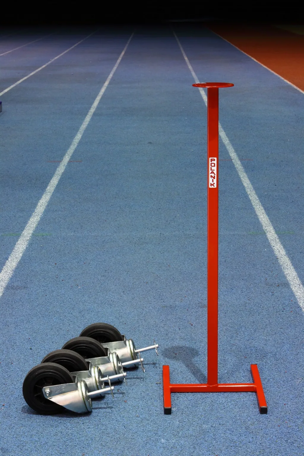 Red metal steeplechase hurdle upright with flat top and four black caster wheels with silver mounts on a blue running track.