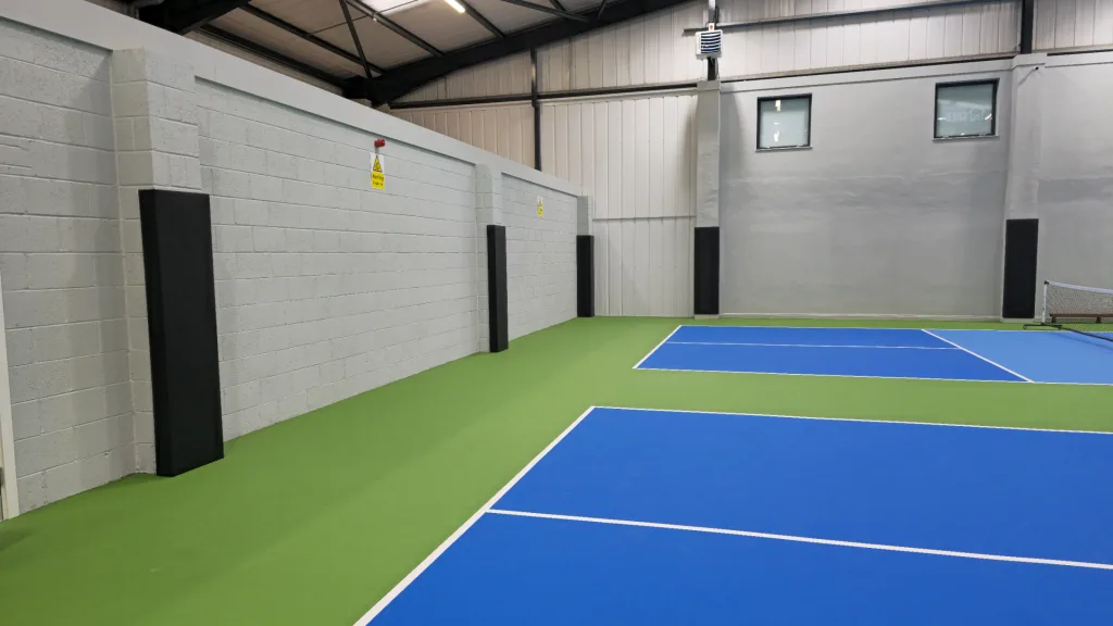 Indoor sports court with blue courts and green surrounds and black square post pads attached to wall pillars.