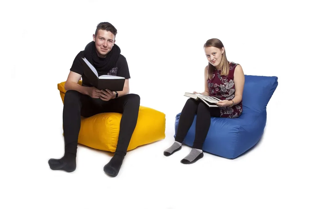 A young man and woman sit reading on polyester bean chairs, one yellow and one royal blue.
