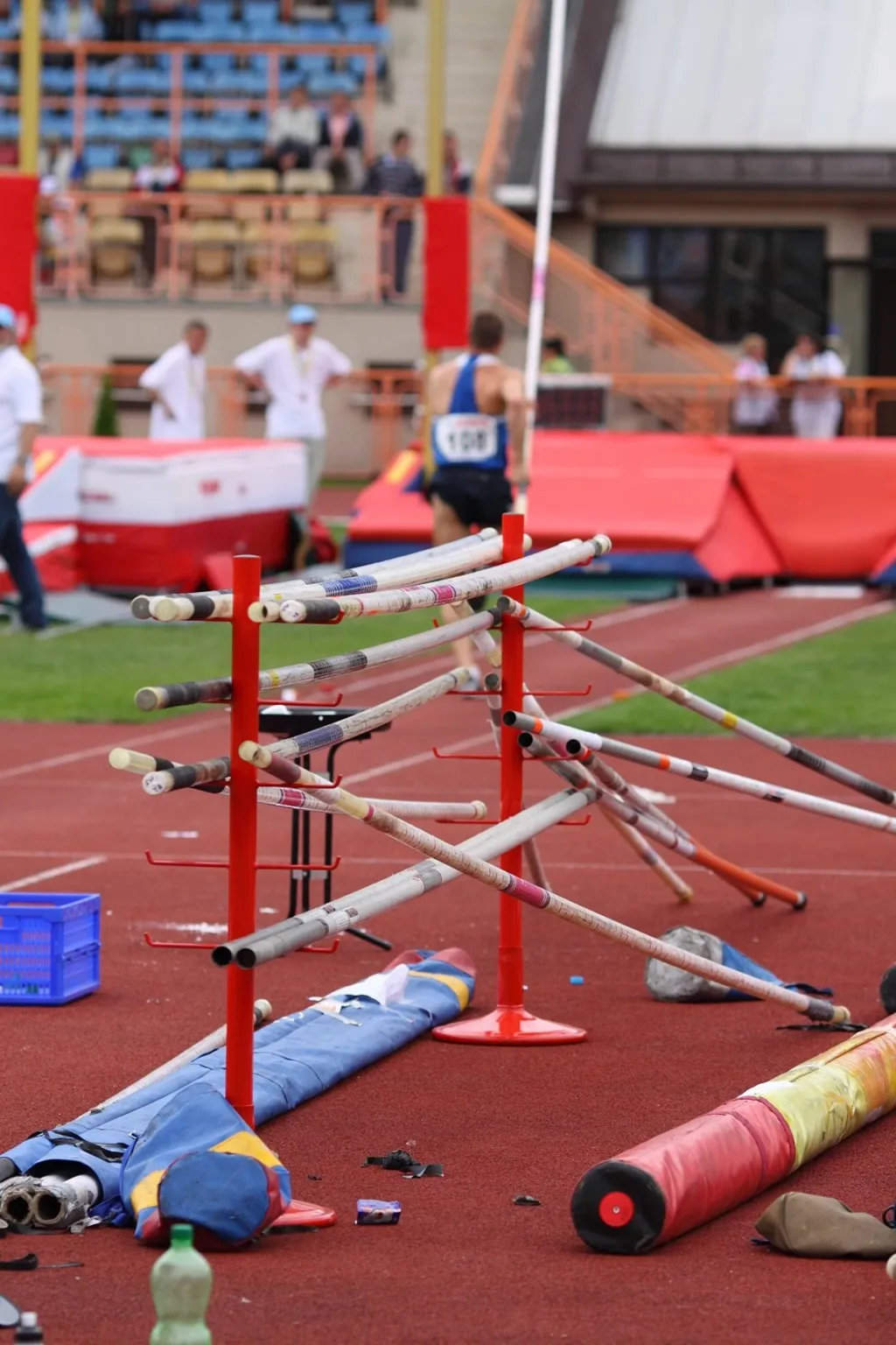 Pole rack made from powder painted steel holding multiple vaulting poles beside a running track and landing mat.