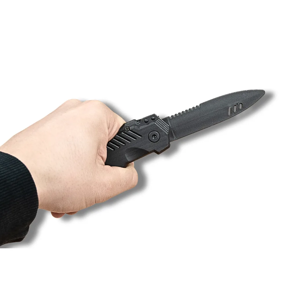 Hand grasping a black realistic retractable training knife with the blade extended.