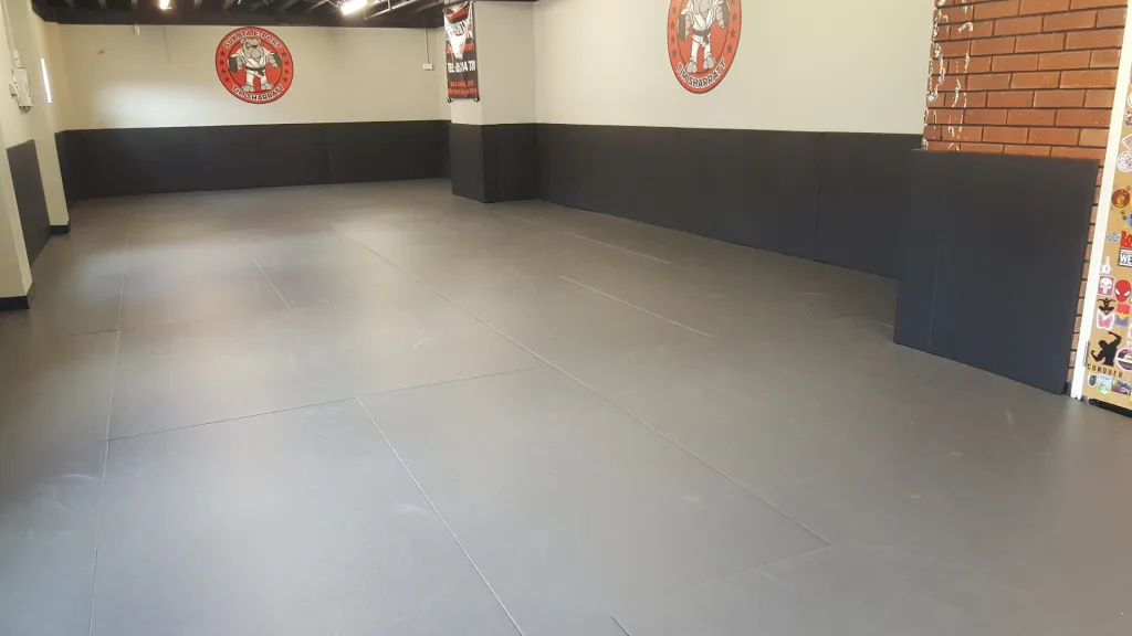 Training room with dark grey combat mats covering the floor and lower walls, smooth polyester PVC surface and heat-sealed seams.