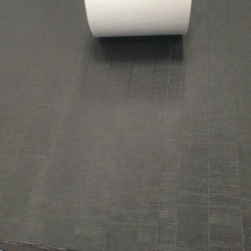 Roll of black tatami tape with its white adhesive backing partially peeled, lying on a textured black mat.