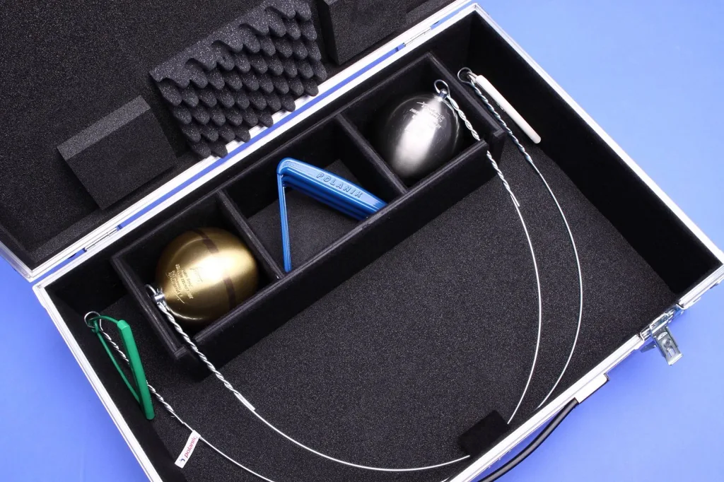 Aluminium transport case open with foam-lined compartments holding two hammer heads, spare handles, and a triangular tool.