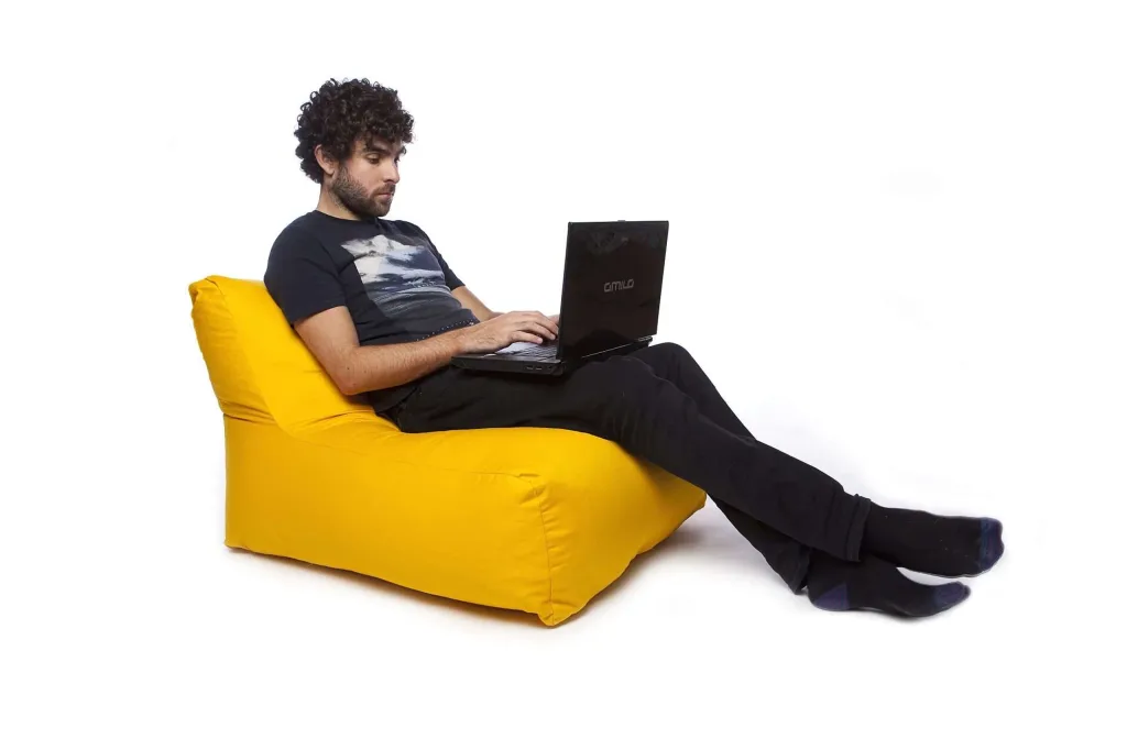 Man reclining on a yellow cotton bean chair using a laptop.