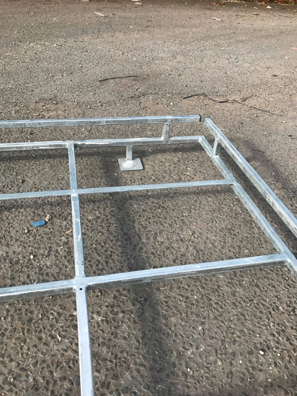 Galvanised steel platform frame for high jump on rough asphalt, showing grid bars, a wide foot plate and a surrounding guardrail.