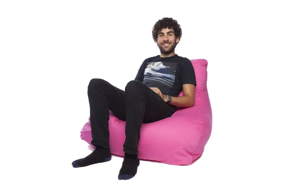 Smiling man in black clothes seated on a pink cotton bean chair with an extended back.