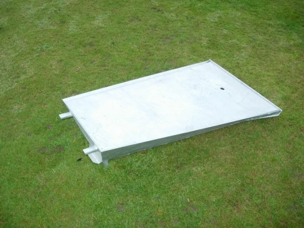Rectangular pole vault trough with lid installed and two short projecting pipes, resting on grass.