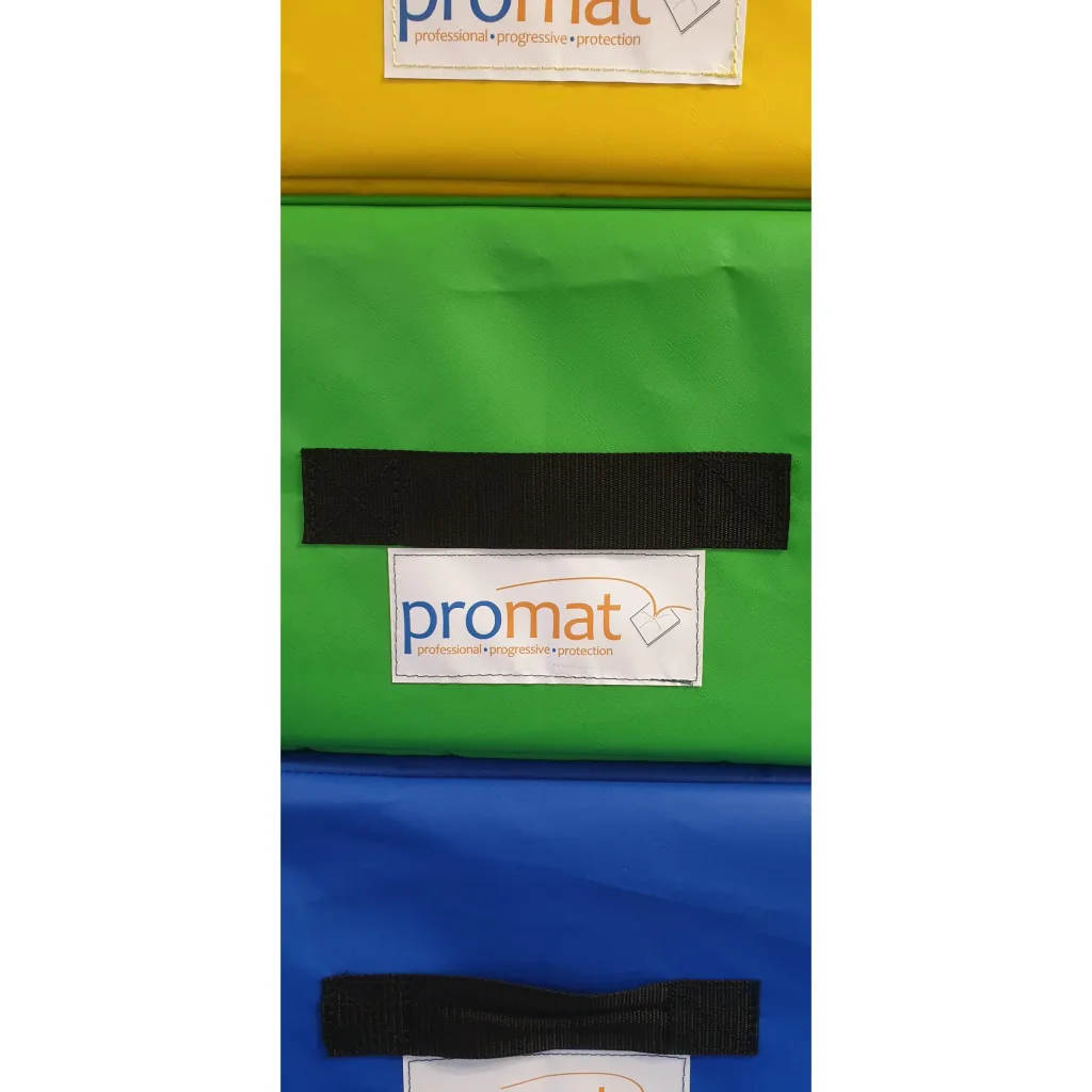 Stacked yellow, green, and blue PVC-covered foam vaulting box sections with black handles and label reading "promat professional • progressive • protection".