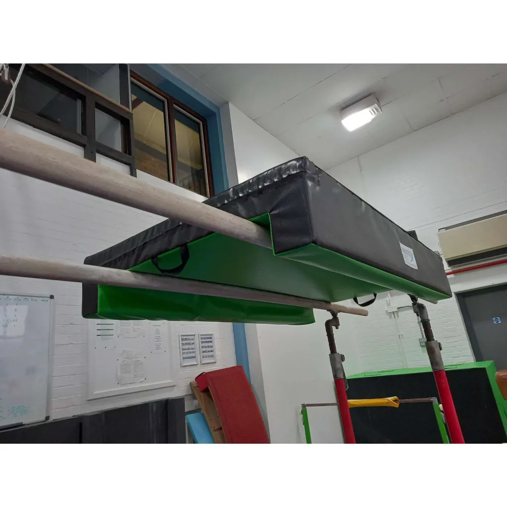 U-shaped parallel bars protection mat with jersey fabric top and nylon-reinforced PVC zipped cover, black top and green underside with carrying handles, draped over wooden bars.