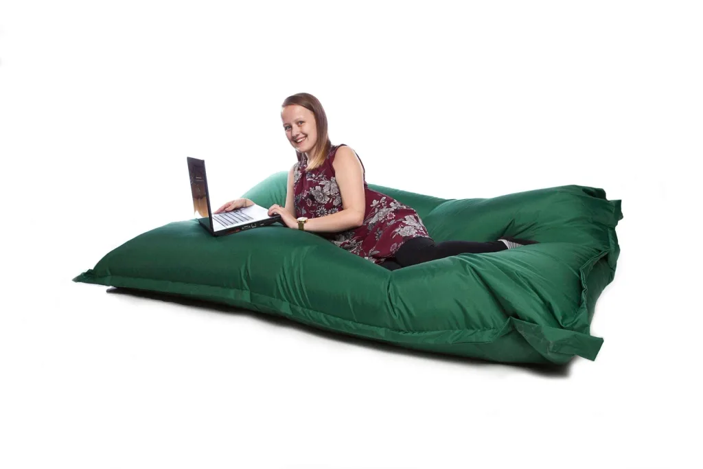 Woman reclining on a large green polyester floor cushion using a laptop.