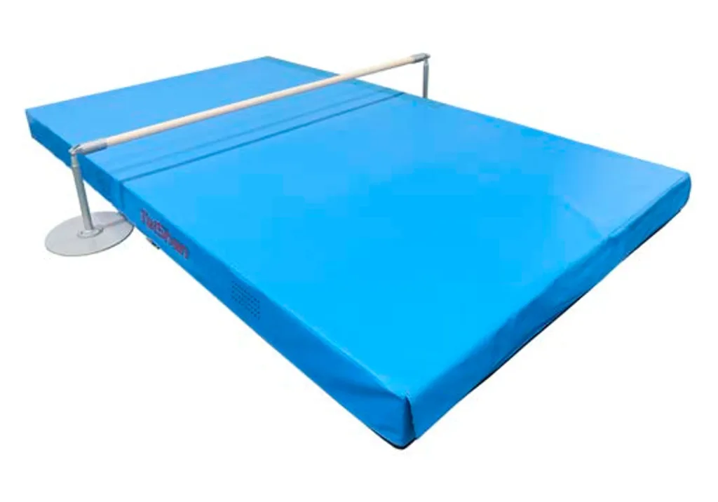 Blue gym landing mat with a maple horizontal bar mounted on powder-coated metal supports with round base plates.