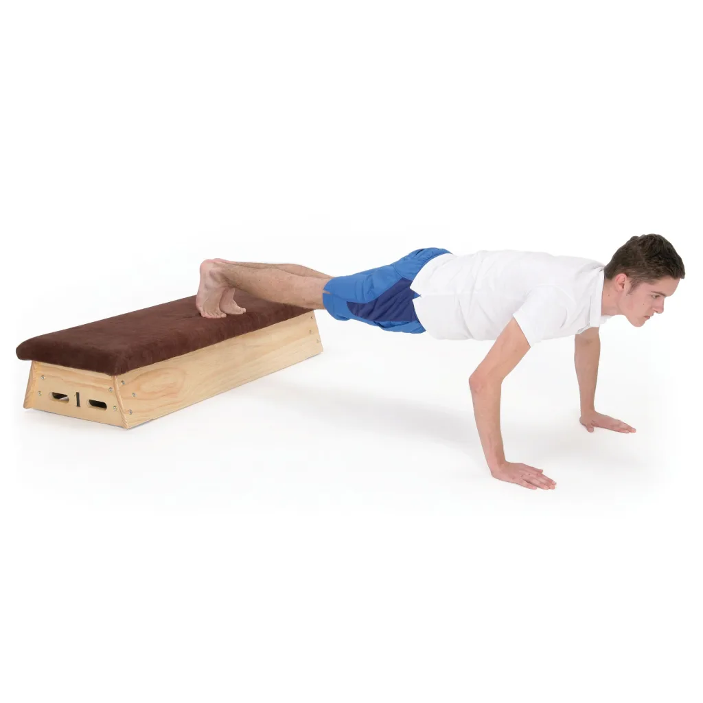 Man in white shirt and blue shorts doing an elevated push-up with feet on a timber vaulting box topped in natural hide.