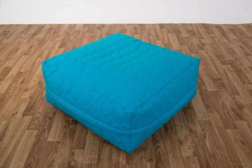 Child square bean bag made of cotton in turquoise, sitting on a wooden floor.