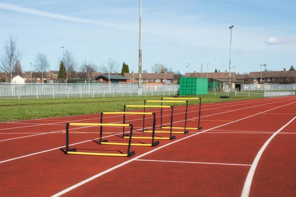 Five yellow-and-black adjustable hurdles lined up on a red outdoor running track.