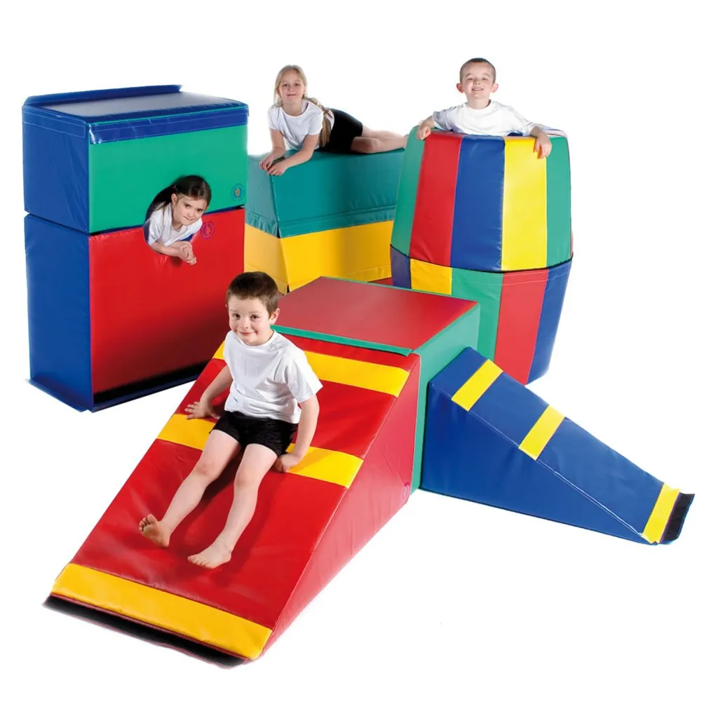 Four children playing on a multicolored foam gym set with a red sloped ramp, yellow stripes, green and blue blocks, and a striped tower.