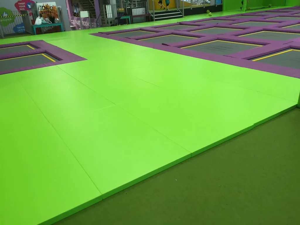 Bright green PVC floor mats surrounding purple-bordered trampoline squares in an indoor trampoline park.