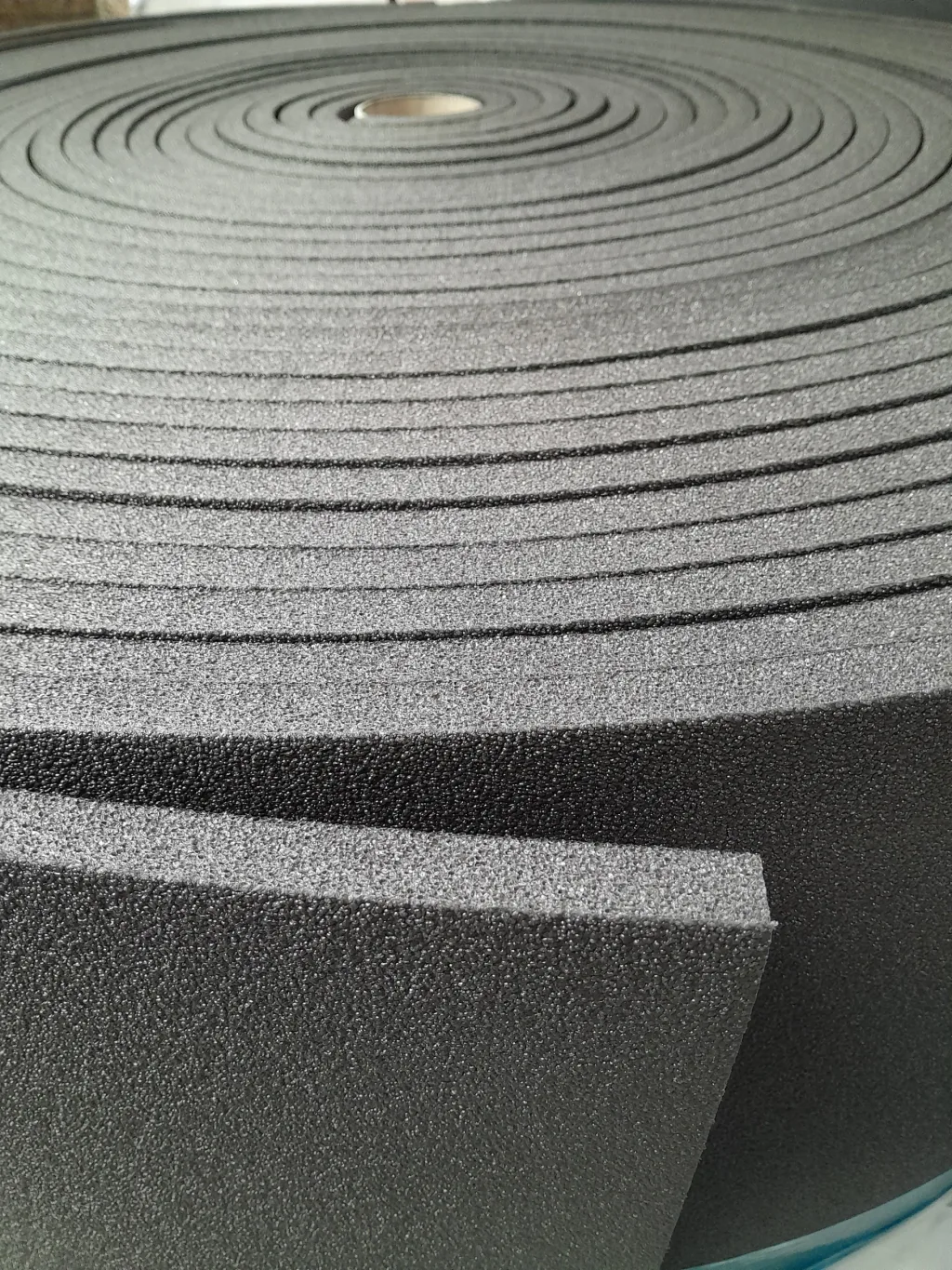 Large roll of grey foam underlay for sprung floors with visible concentric spiral layers and a squared cut edge.