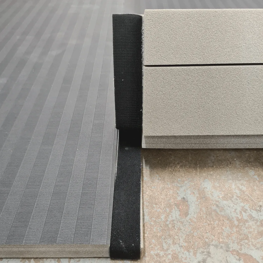 PVC roll-out mats with low-profile tatami emboss joined by a black hook-and-loop strip, showing a seam between panels on a concrete floor.