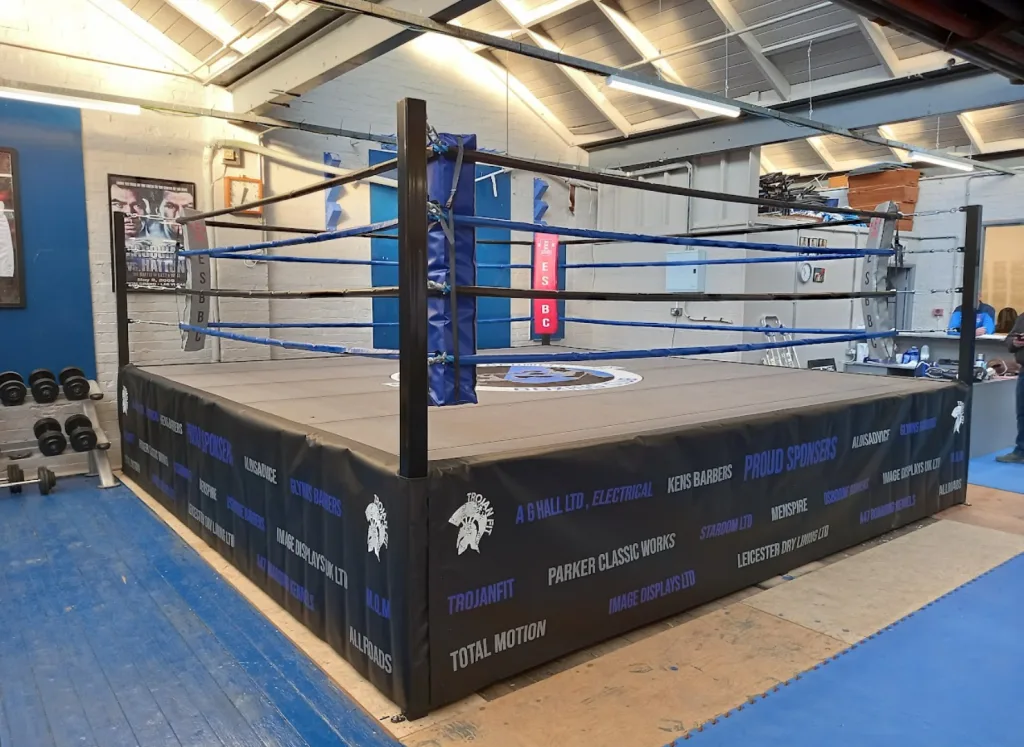 Competition ring with steel frame and powder-coated posts, blue ropes and a custom-branded black skirt with sponsor names.