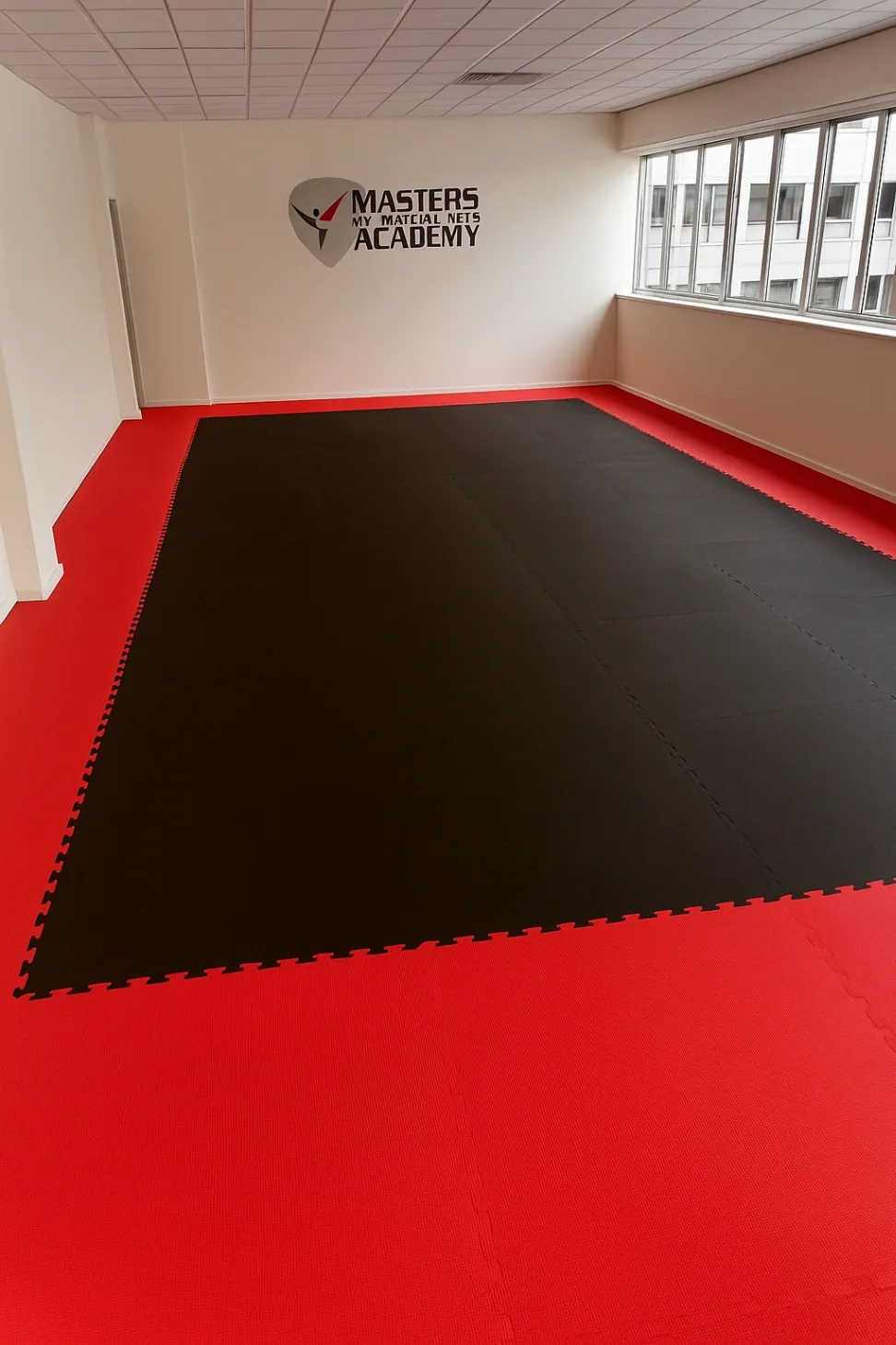 Training room with black and red interlocking jigsaw mats, white walls, windows, and wall logo reading "MASTERS MY MARTIAL ARTS ACADEMY".