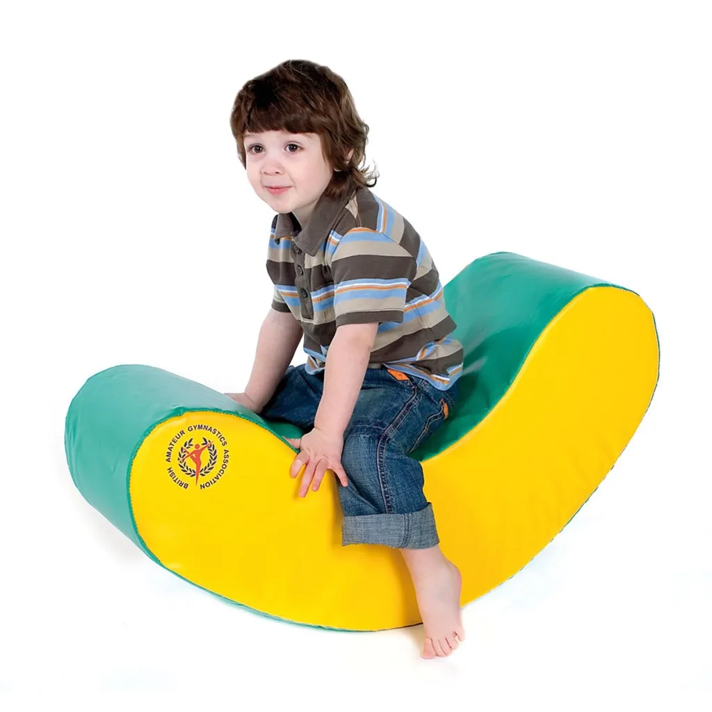 Young child sitting on a yellow and green curved soft play rocker, logo reads British Amateur Gymnastics Association.