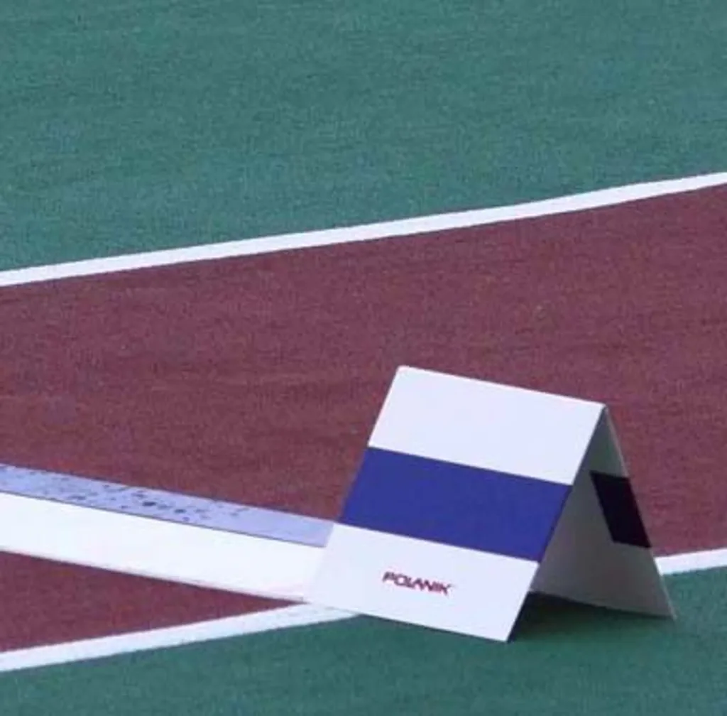 White triangular take-off marker with a blue horizontal stripe sitting on a maroon and green running surface beside white lines.