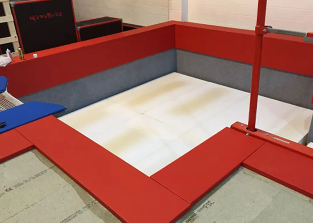 Red-padded rectangular foam pit with gray inner walls, white floor panels and a red support post, with a black box labeled MODUBLOX in the background.