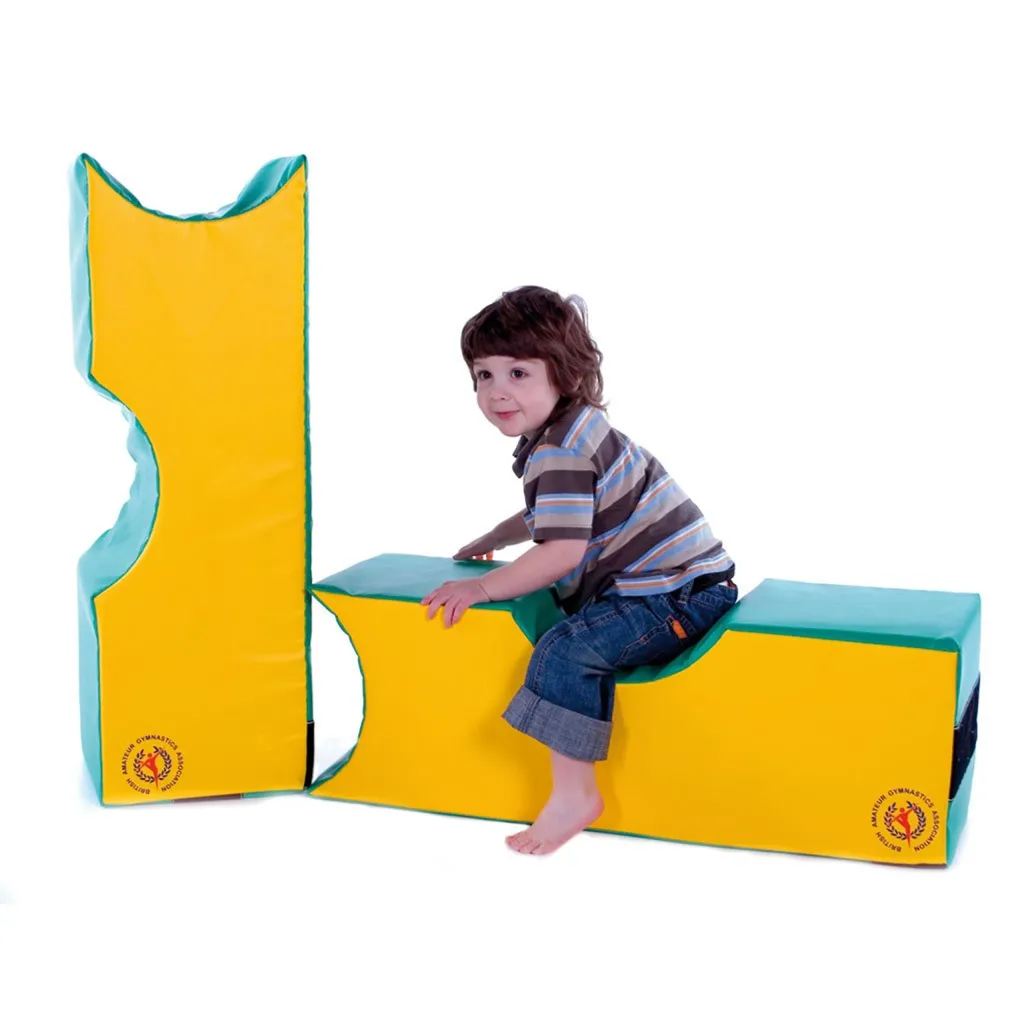 Young child sitting on yellow and green foam play blocks with curved notches, assembled into an L-shaped play structure.