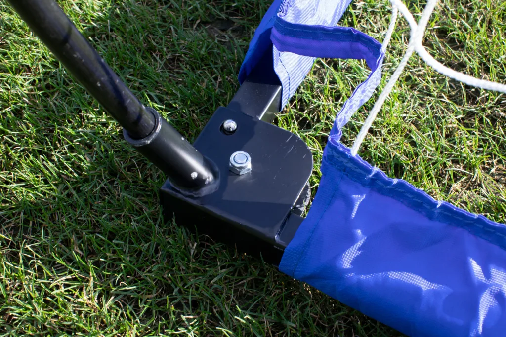 Black metal goal base with angled pole, blue fabric sleeve and white netting resting on green grass.