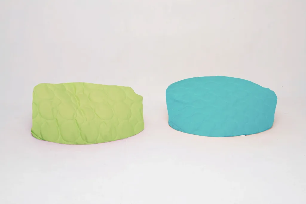 Two padded child pie bean bags on a white background, lime green on the left and turquoise on the right, with circular quilted stitching.
